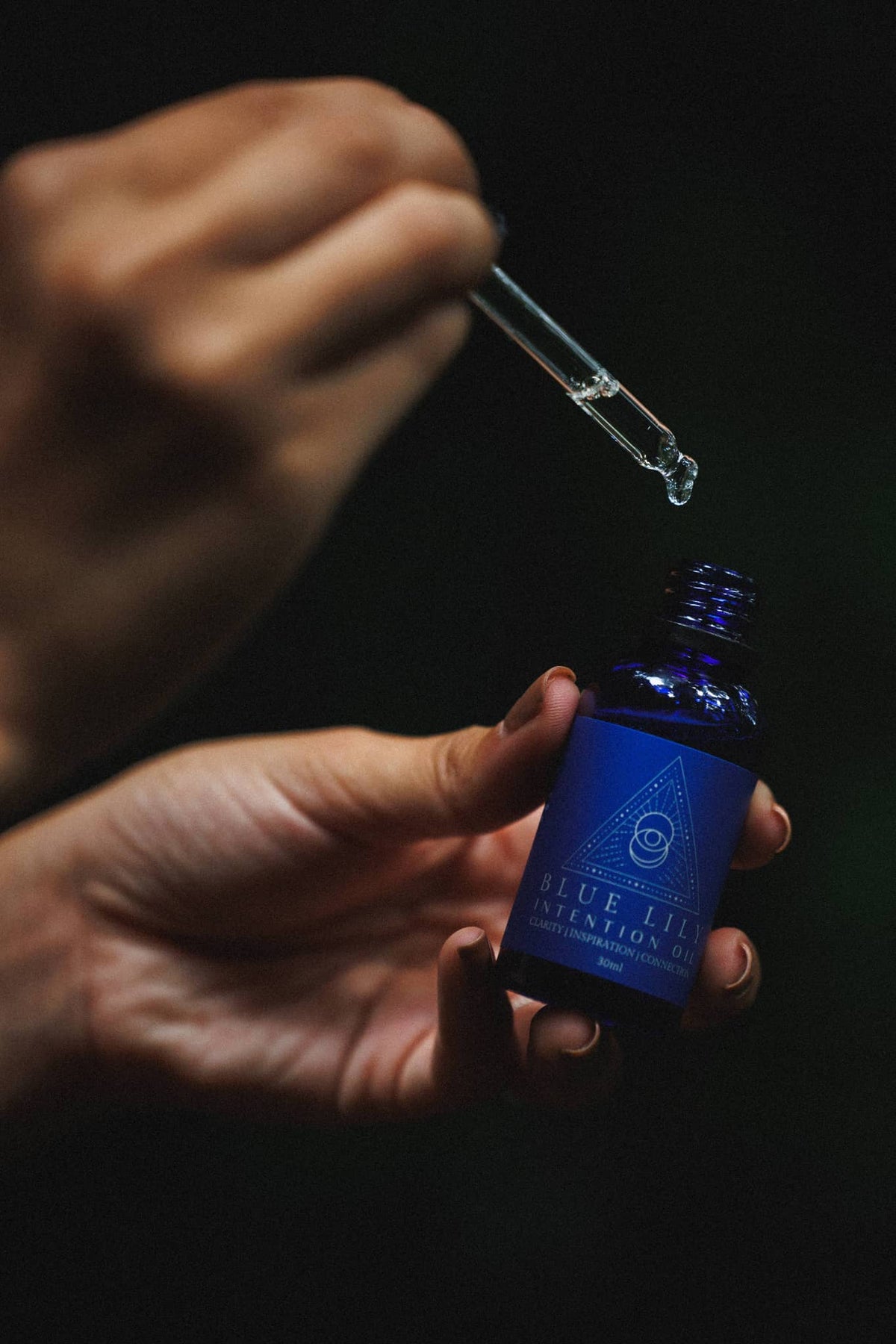 Blue Lotus Intention Oil in a blue glass bottle with dropper held over the hand, perfect for spiritual rituals