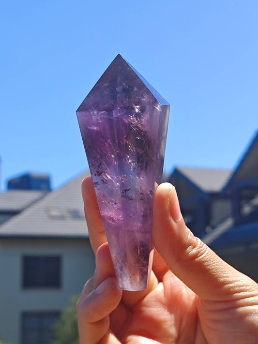Handheld Natural Brazilian Amethyst Wand with a Stunning Purple Crystal Point Against a Clear Sky