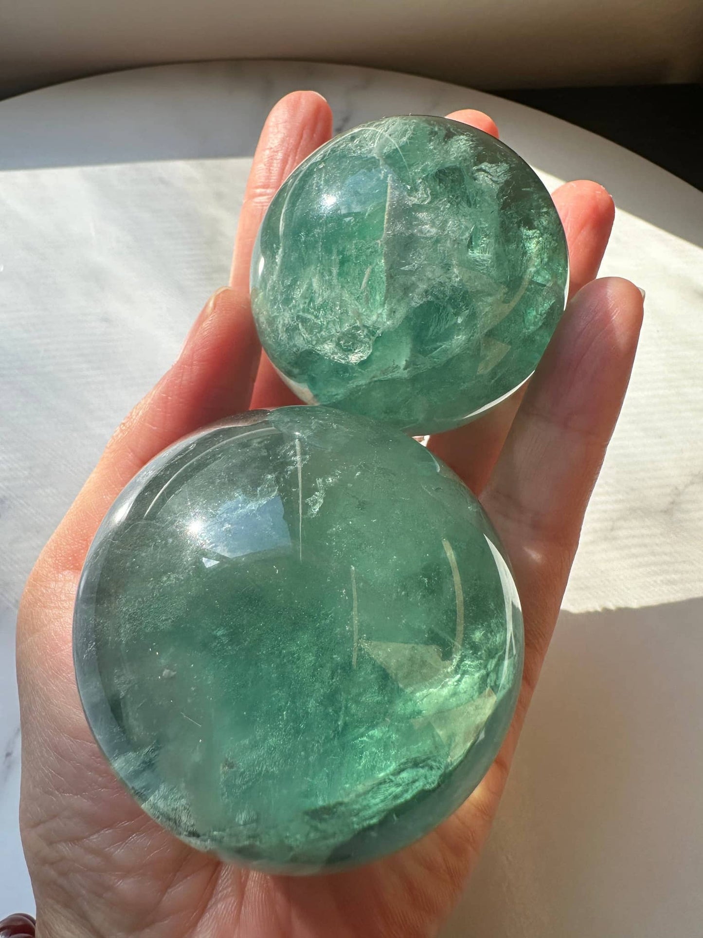 Two Natural Green Fluorite Spheres held in hand, showcasing their vibrant green color and clear surface details