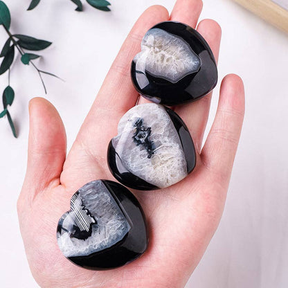 Hand holding three Black Agate Heart stones showcasing unique patterns and smooth surfaces