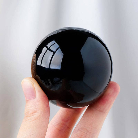 Hand holding a polished Black Obsidian Sphere, showcasing its smooth surface and deep black color