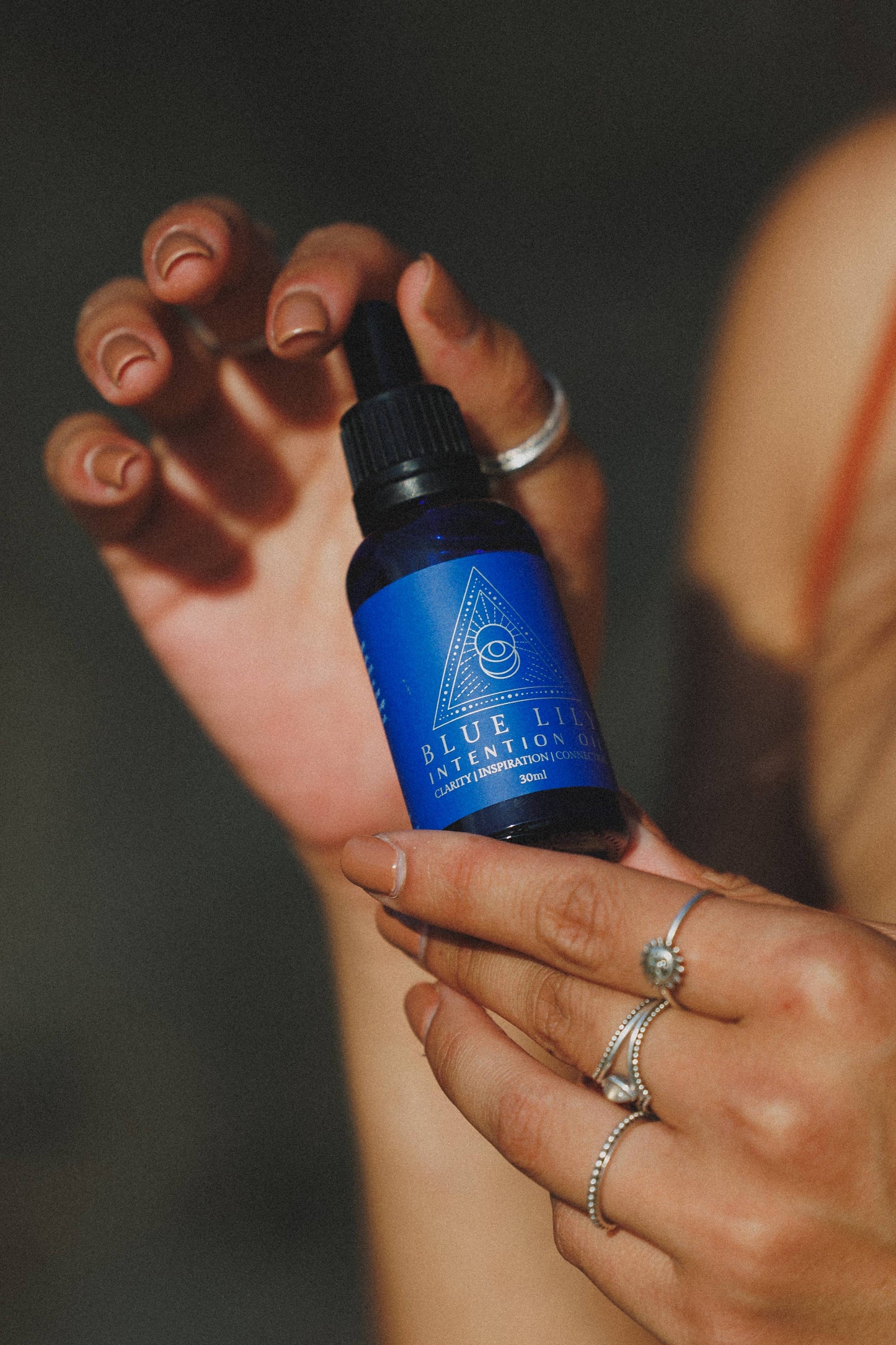 Blue Lotus Intention Oil in a dropper bottle, held in a hand adorned with rings