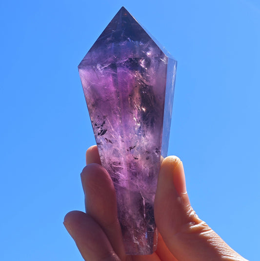 Handheld Natural Brazilian Amethyst Wand with Rich Purple Color Against a Blue Sky