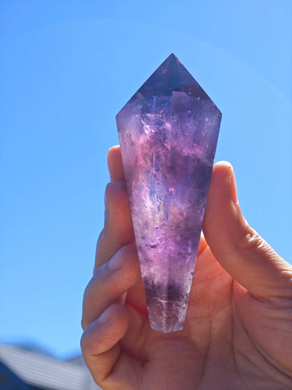 Natural Brazilian Amethyst Wand held in hand under clear blue sky showcasing its purple hues and pointed shape
