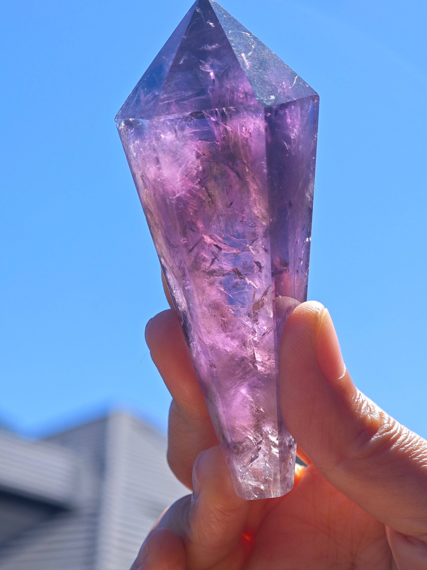 Natural Brazilian Amethyst Wand held in sunlight, showcasing its translucent purple hues and unique crystal facets
