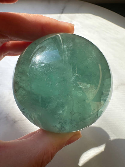 Person holding a Natural Green Fluorite Sphere capturing light reflections and unique textures