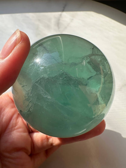 Hand holding a Natural Green Fluorite Sphere with a smooth, polished surface and soft green tones