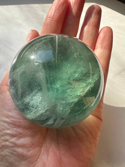 Natural Green Fluorite Sphere held in a hand, showcasing its smooth surface and rich green hues