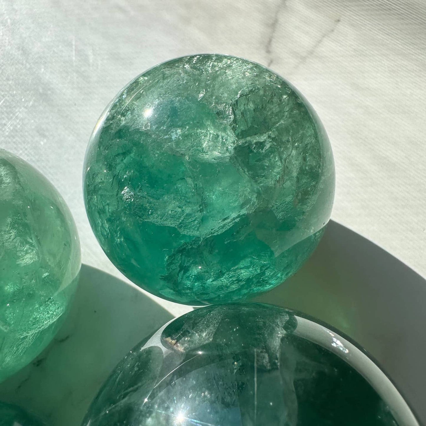 Natural Green Fluorite Sphere showcasing vibrant teal hues and crystal clarity on a white surface