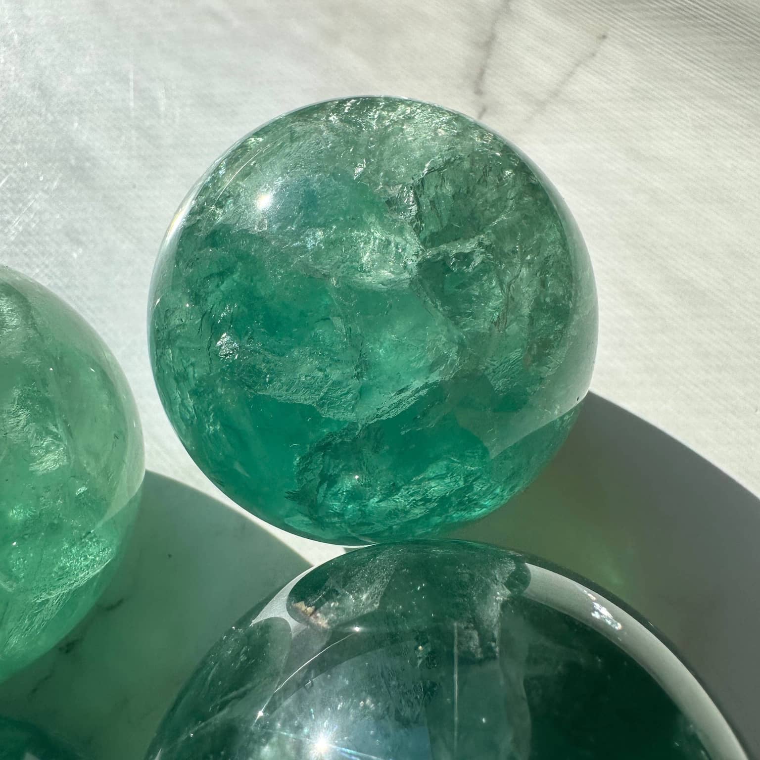 Natural Green Fluorite Sphere showcasing vibrant teal hues and crystal clarity on a white surface